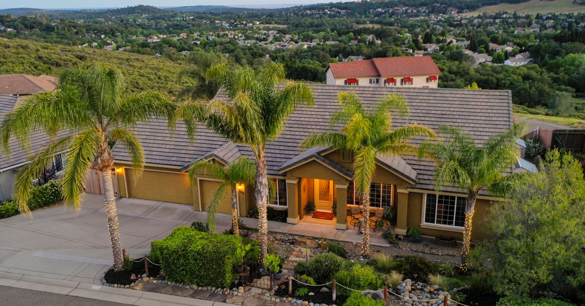 Aerial view of a beautiful suburban home surrounded by lush greenery and palm trees.
