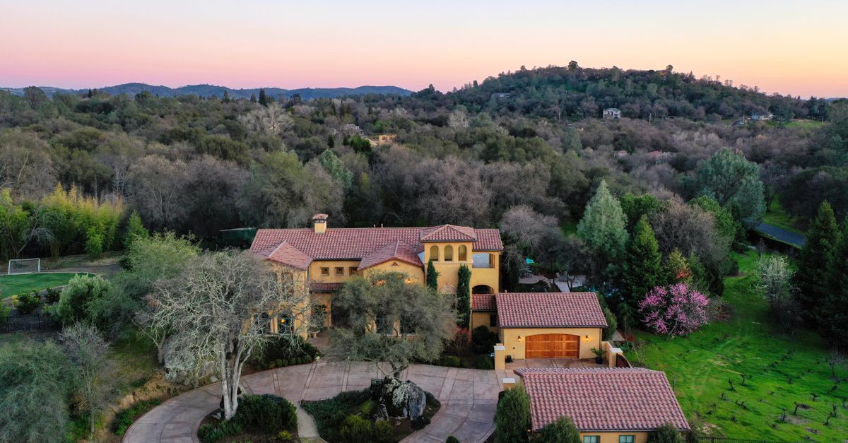 Aerial view of a luxury villa surrounded by lush greenery and hills during sunset.