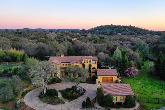 Aerial view of a luxury villa surrounded by lush greenery and hills during sunset.