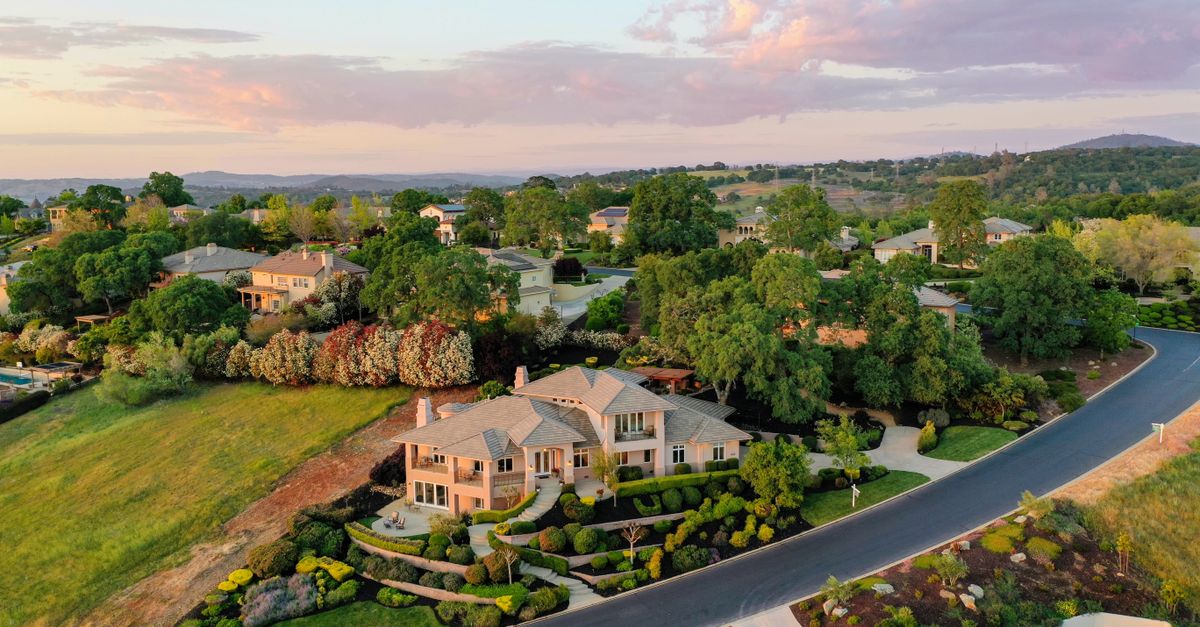 Aerial shot of elegant suburban houses with lush gardens during sunset.