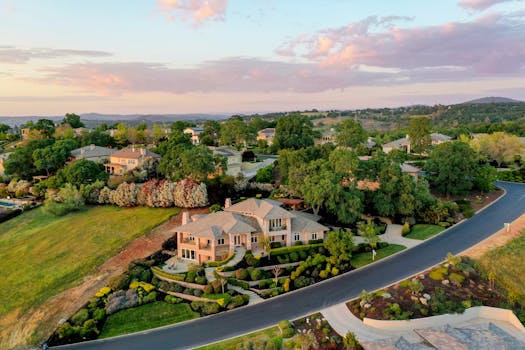 Aerial shot of elegant suburban houses with lush gardens during sunset.