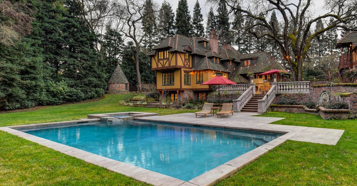 Stunning Tudor-style mansion with a pool, lush garden, and vibrant summer scenery.