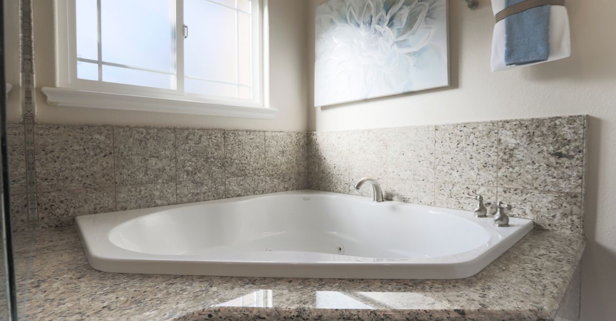 Spacious contemporary bathroom featuring a corner bathtub, granite tiles, and elegant decor.