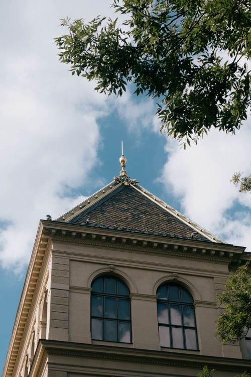 Free Low angle view of a classic urban building with decorative roof, framed by trees and sky. Stock Photo
