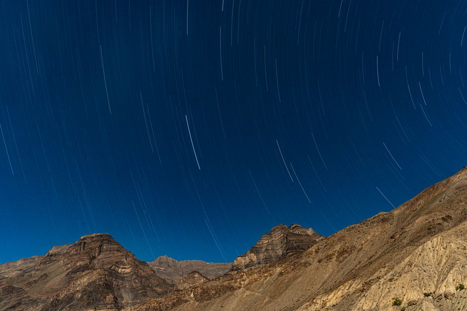 Star trails illuminate the clear night sky over rocky mountains in Kaza, HP, India, showcasing a mesmerizing celestial phenomenon.