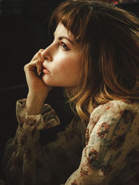 A thoughtful woman in a vintage floral dress, captured in dramatic lighting for a classic and romantic feel.