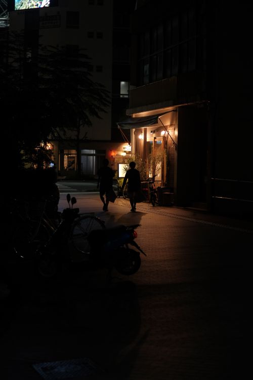 Free Silhouettes walking by illuminated city street at night, capturing urban ambiance. Stock Photo