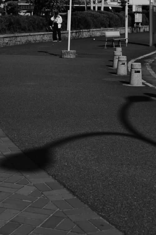 Free Black and white photo of an empty city street with dramatic shadows and a lone pedestrian. Stock Photo