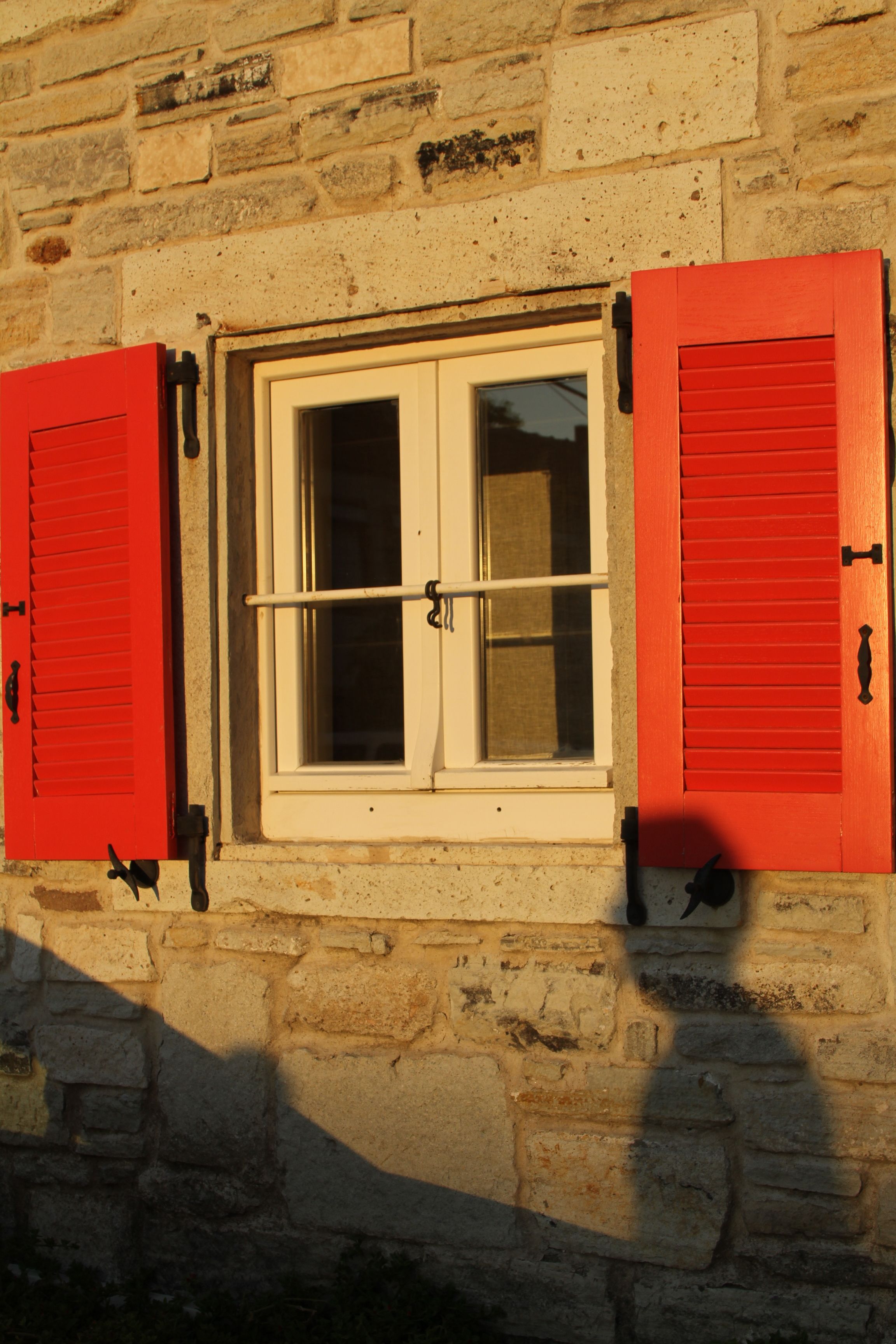Stone building with red shutters and window in Foça, Türkiye.