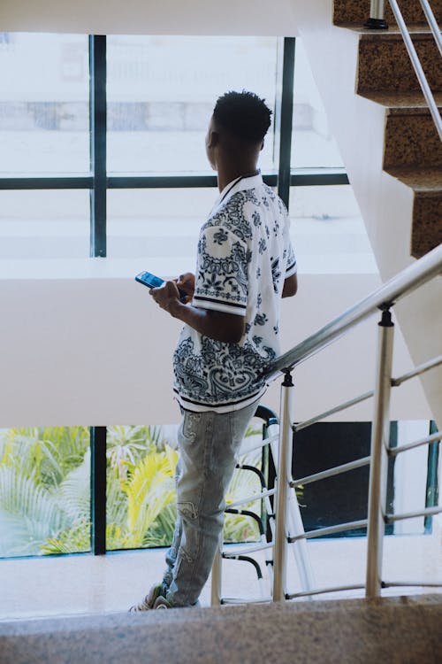 Man Texting and Looking Outside Standing on Staircase
