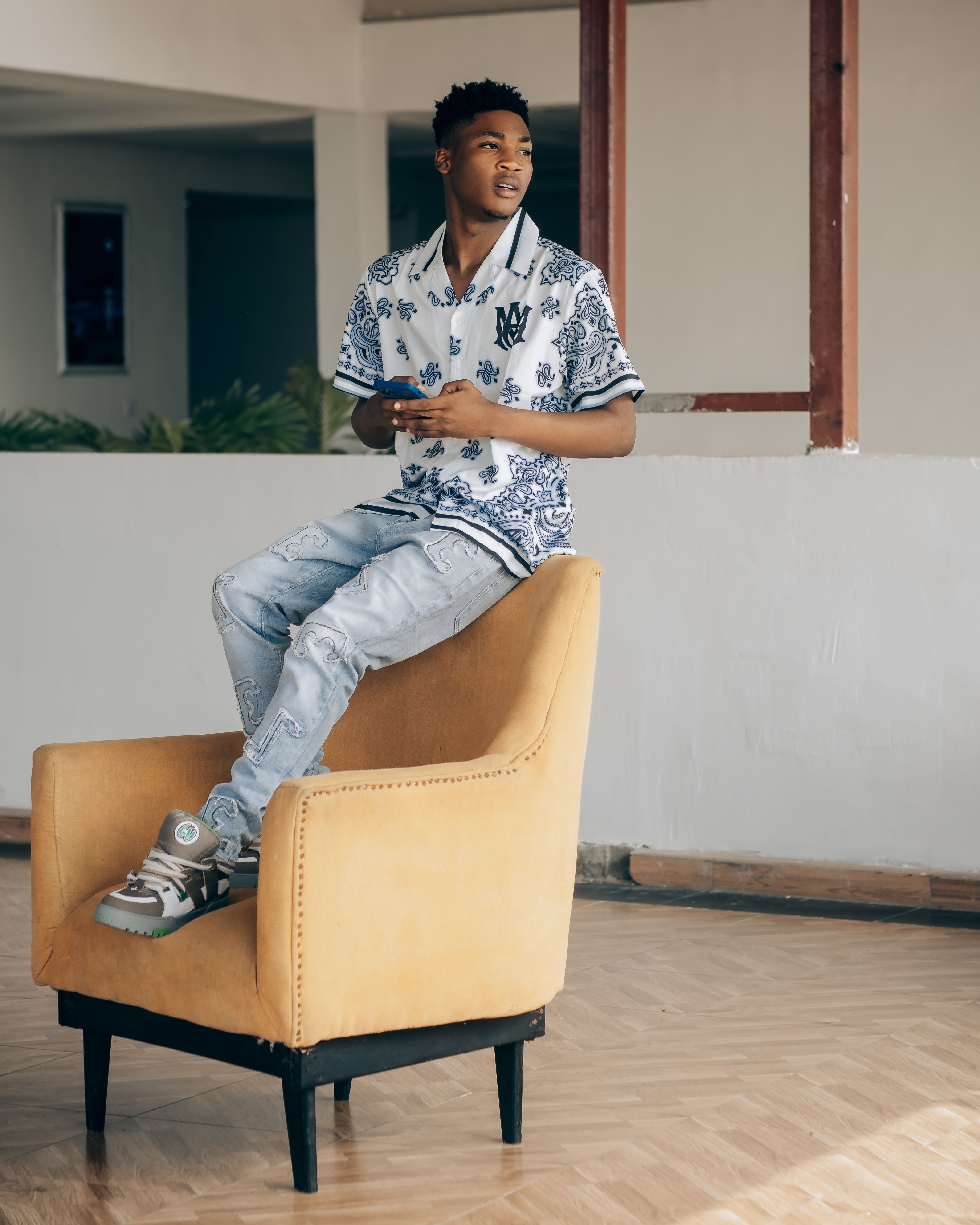 Fashionable young man sitting on a yellow chair in a modern indoor setting.