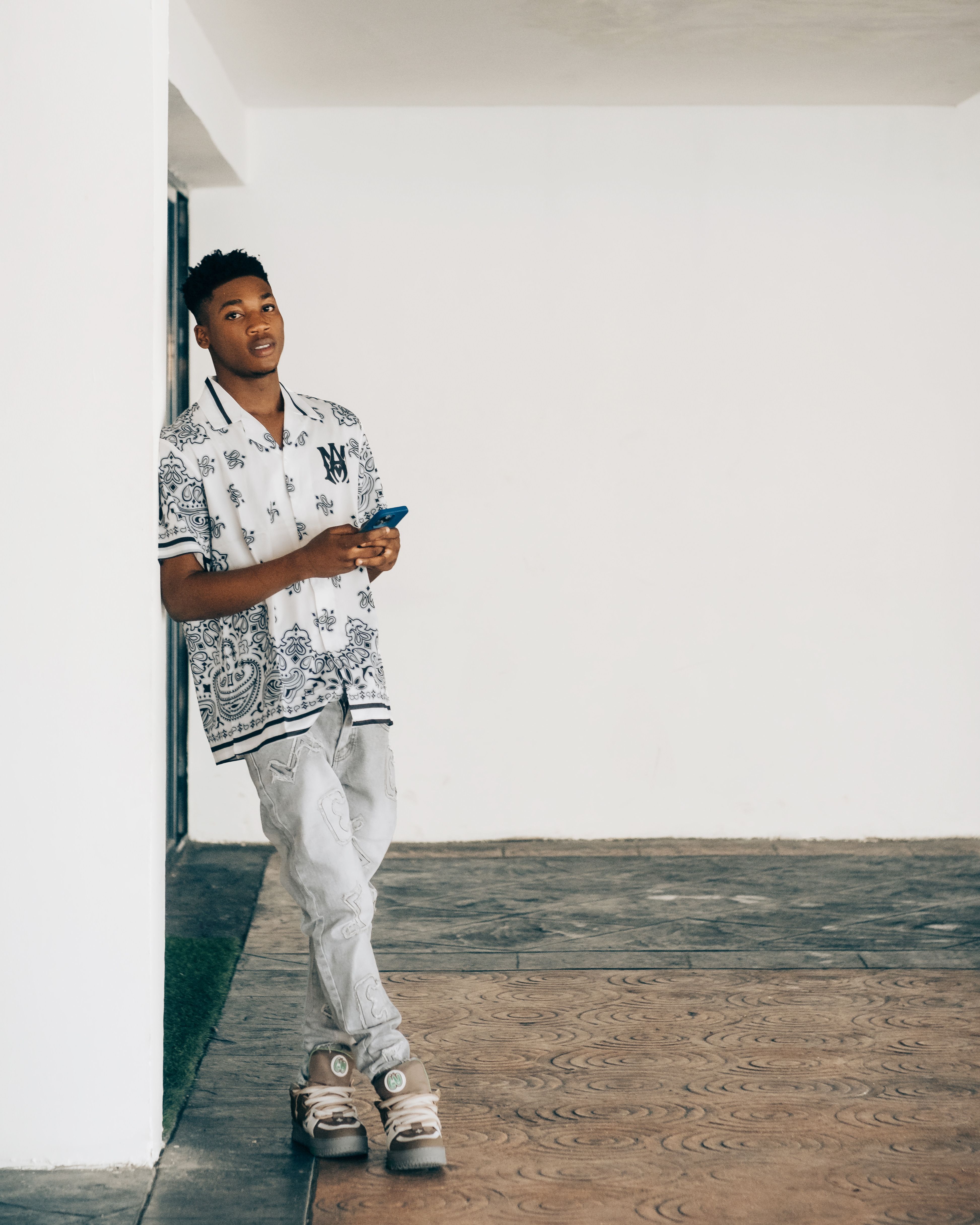 Young adult leaning stylishly against a white wall indoors, exuding a trendy and relaxed vibe.