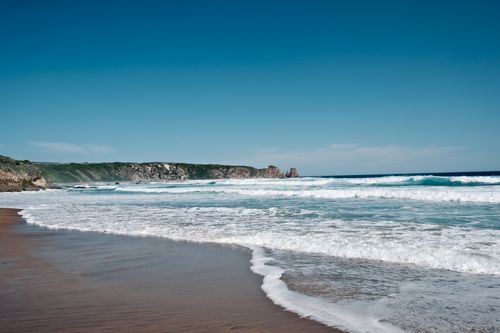 Free Serene coastal scene featuring a sandy shore, gentle waves, and clear blue skies. Stock Photo
