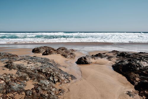 Free A tranquil beach scene with eroded rocks and gentle waves under a clear sky. Stock Photo