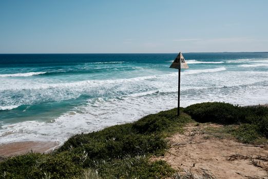 A tranquil coastal scene with waves crashing on the shore and a cliffside sign under a clear sky.
