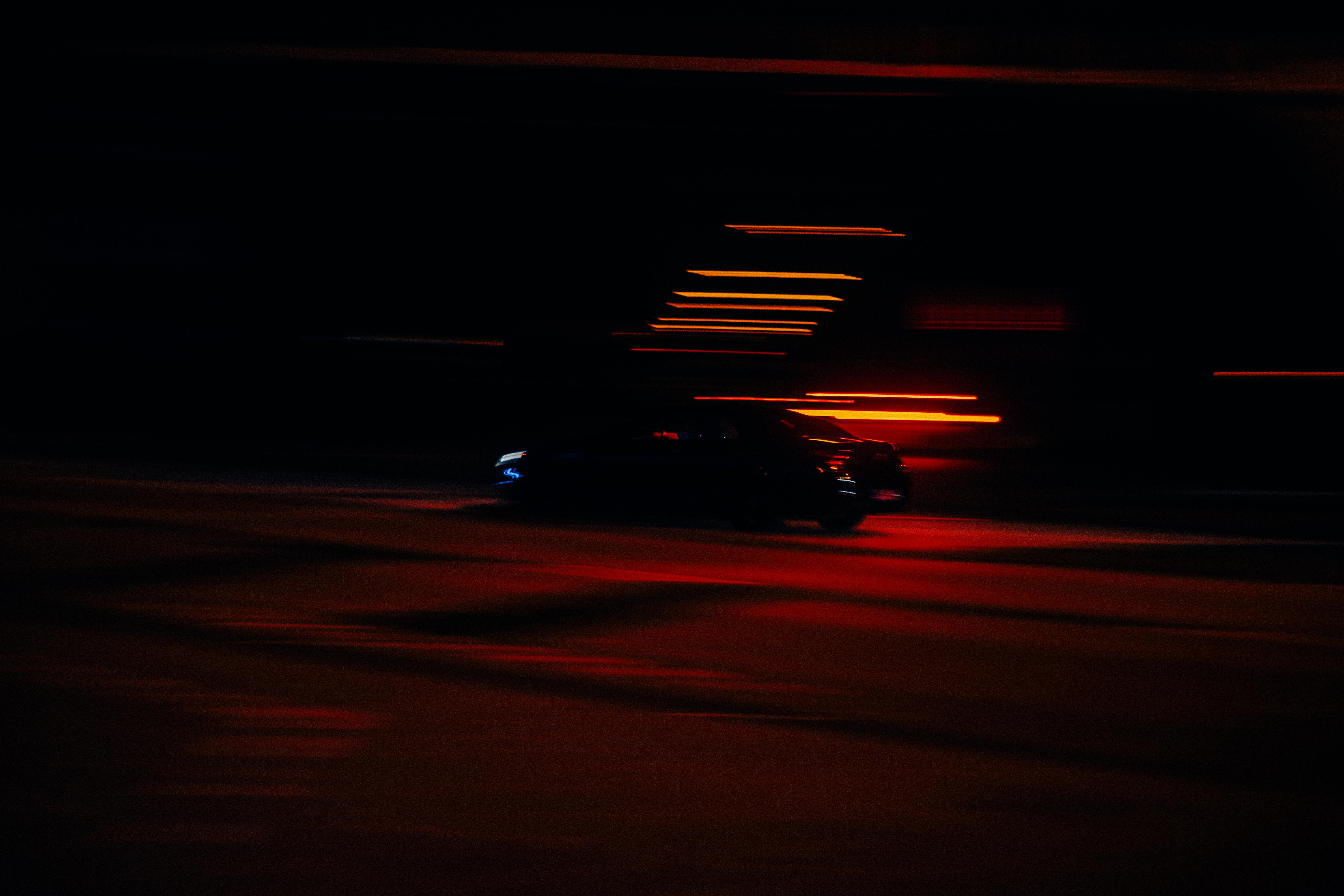 Blurred image of a speeding car at night in an urban setting with streaks of red light.