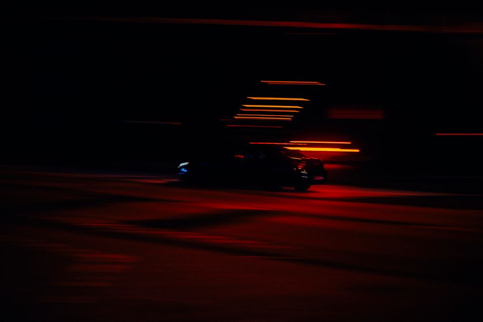 Blurred image of a speeding car at night in an urban setting with streaks of red light.