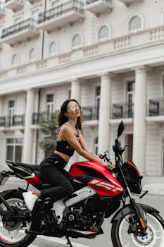 Fashionable woman in sunglasses sitting on a motorcycle in front of an elegant building in Baku, Azerbaijan.