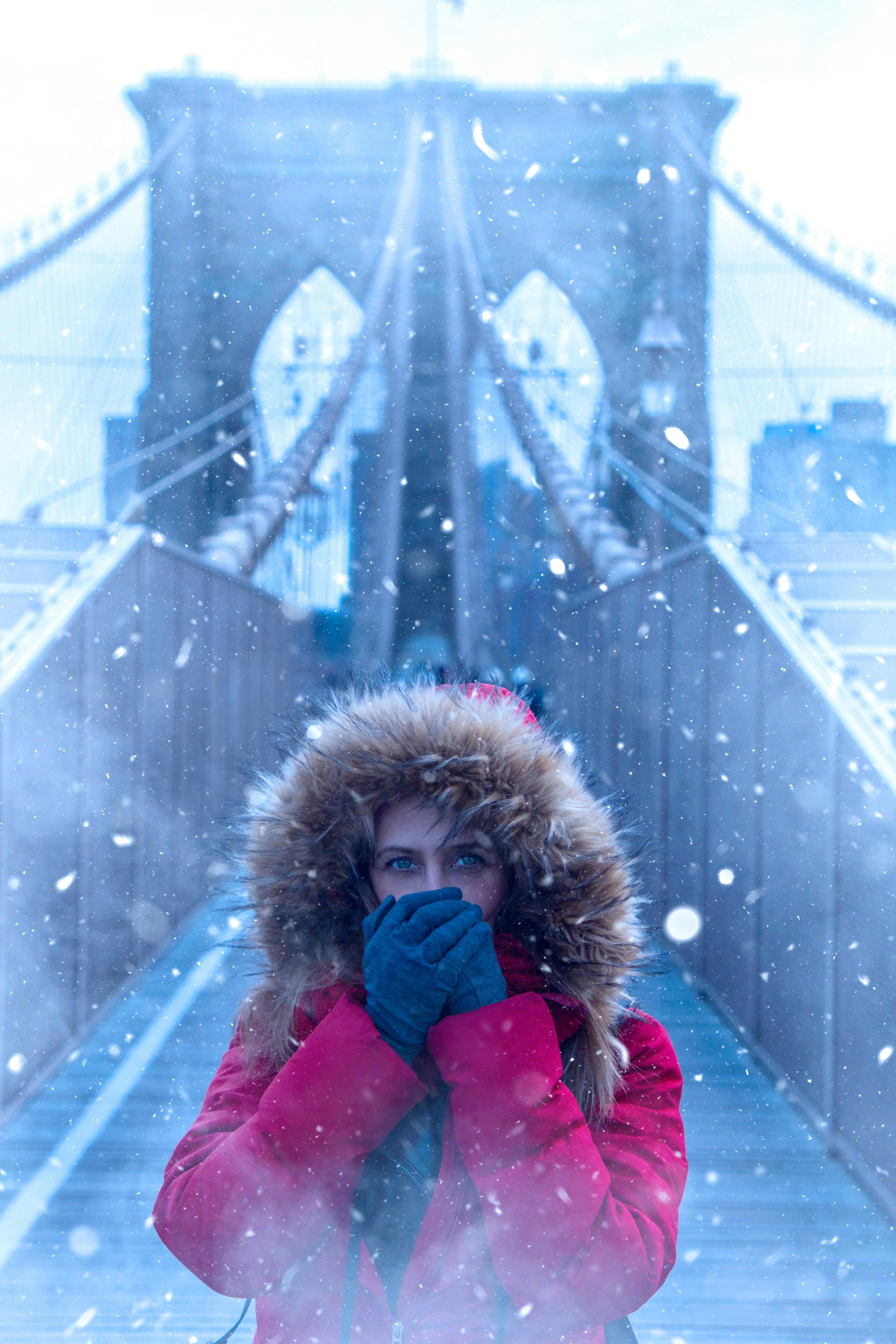 woman wearing red parka jacket while standing on brooklyn bridge