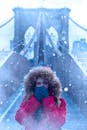 冬天，纽约市布鲁克林桥上，一位穿着红色外套的女子站在白雪皑皑的桥上