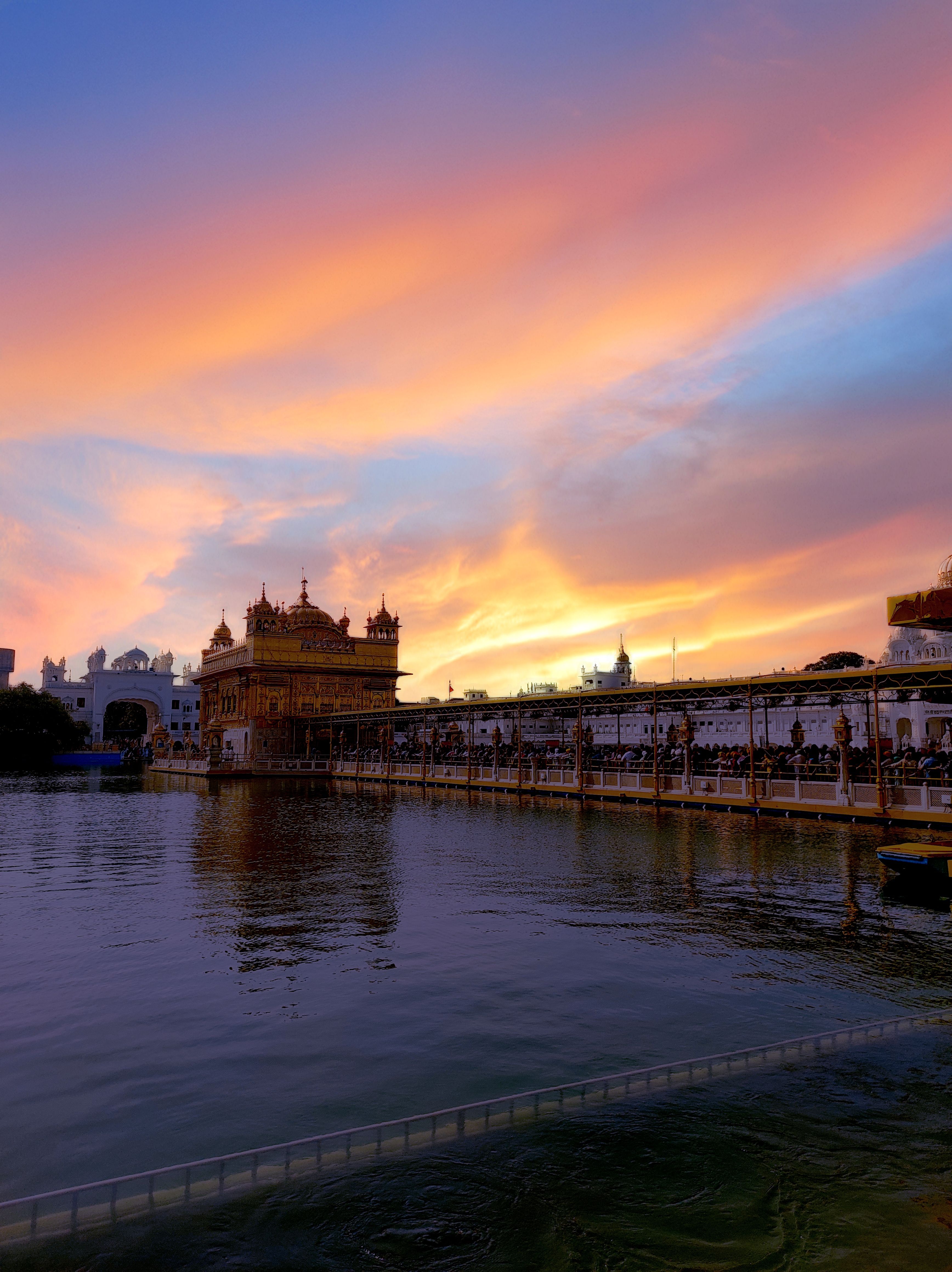Captivating view of the Golden Temple reflecting on water during a vibrant sunset in Amritsar, India.
