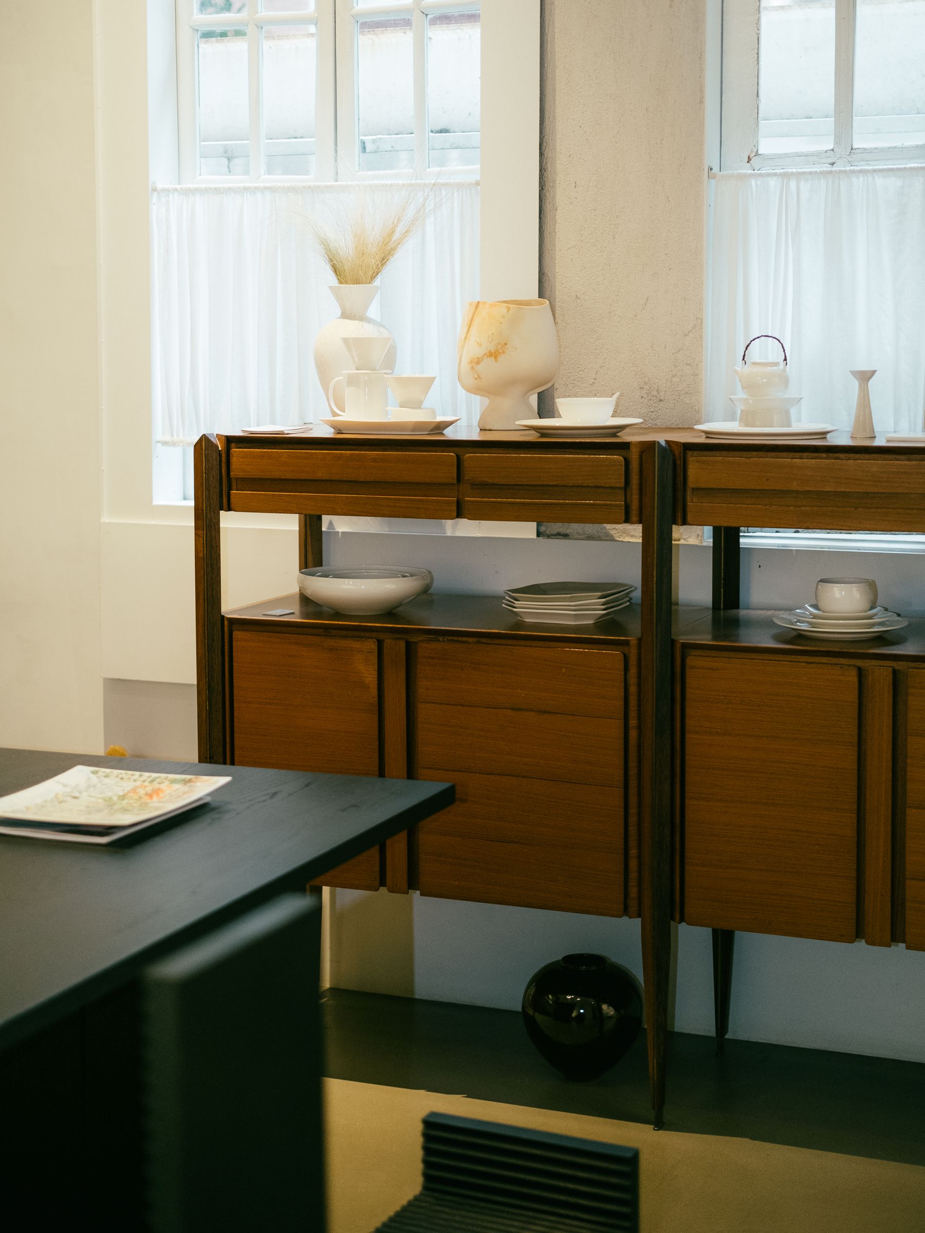 Wooden storage units on slender dark legs displaying white bowls and serving pieces