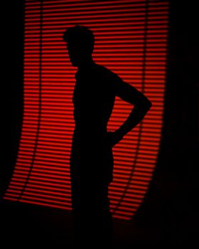 A dramatic silhouette of a person with a red striped light background creating a striking contrast.
