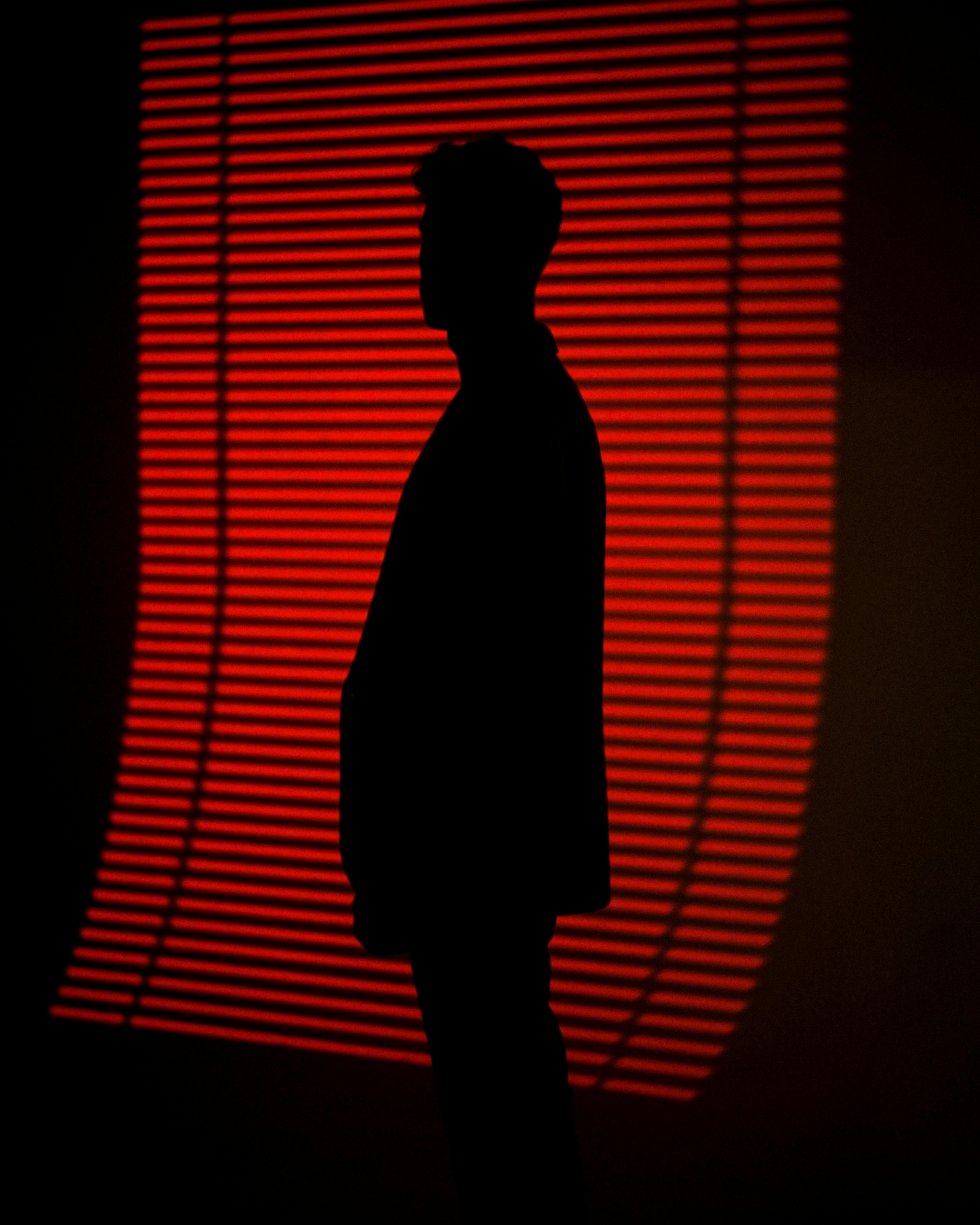 A silhouette of a person standing in front of a striking red light backdrop with horizontal lines.