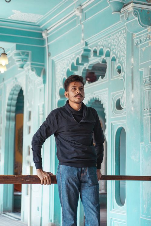 Free A young man standing indoors against a backdrop of ornate historical architecture with intricate patterns. Stock Photo
