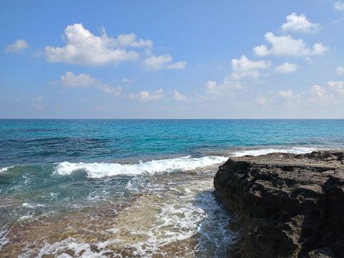 Free Peaceful seascape capturing crystal clear waves crashing on rugged rocks under a bright blue sky. Stock Photo