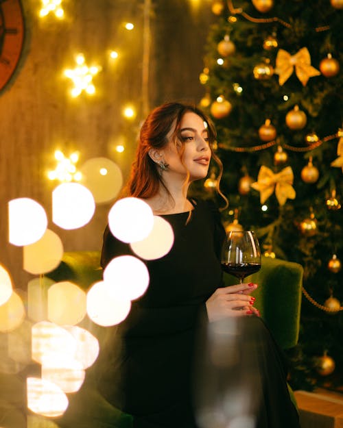 A woman in a black dress is sitting in front of a christmas tree