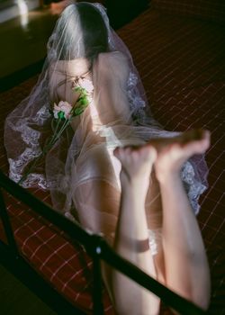 Sensual image of a woman lying in sheer lace lingerie on a bed, holding flowers.