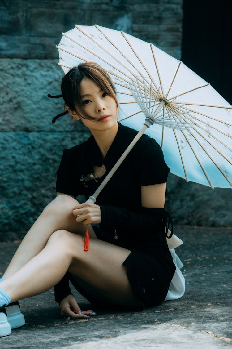 Brunette Woman With Umbrella Sitting On Pavement