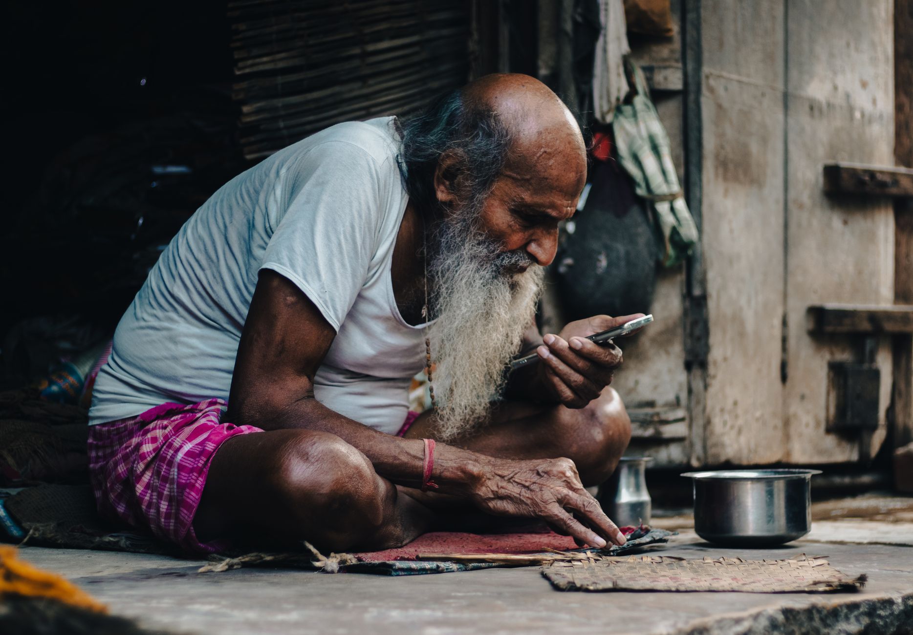Senior man with a beard using a smartphone while sitting outside in Vrindavan, India.