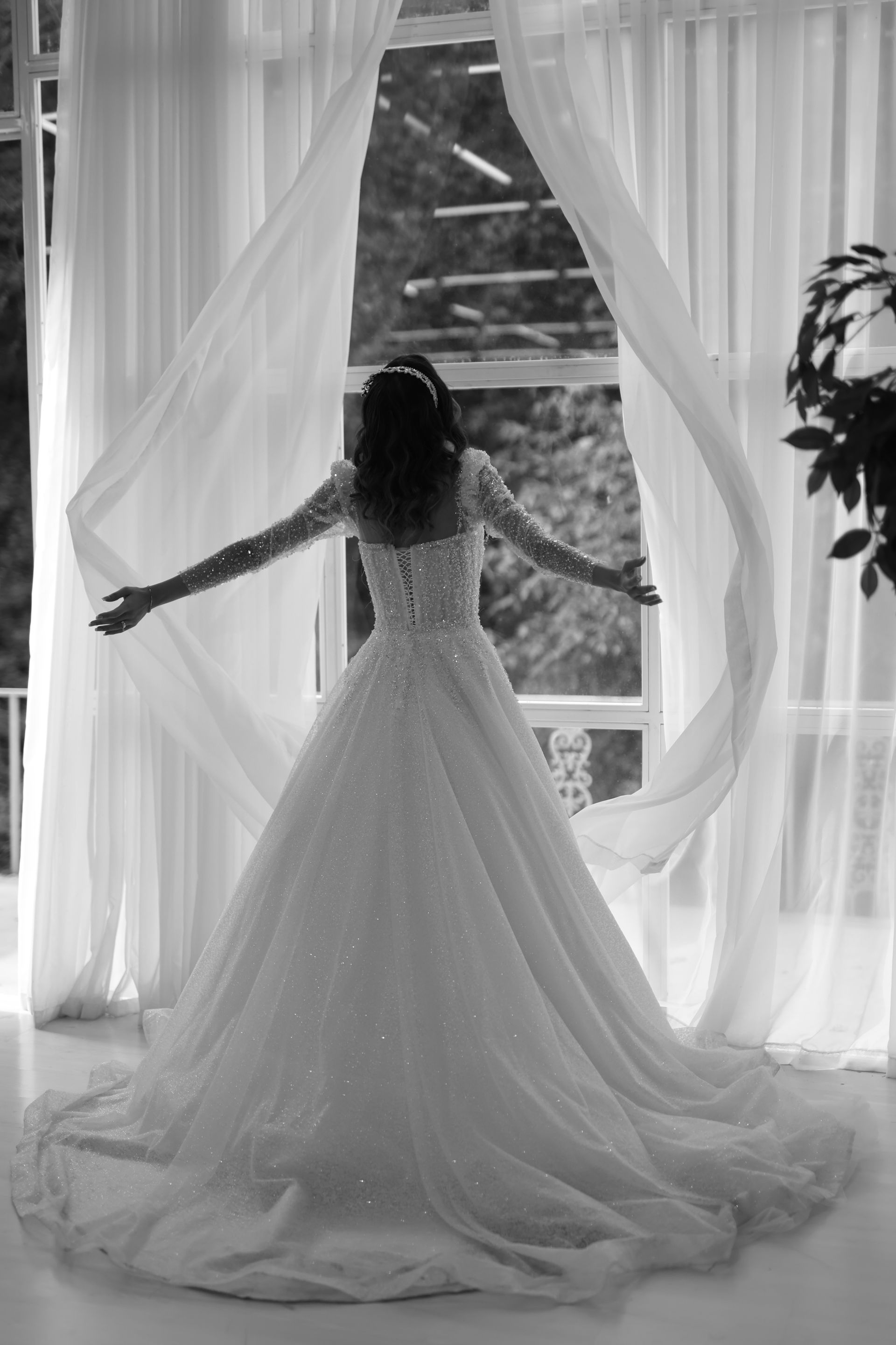 Pengantin dalam gaun perkahwinan yang anggun berdiri di tingkap.