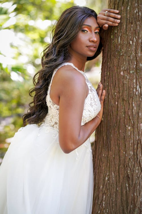 A beautiful black woman in a white dress leaning against a tree