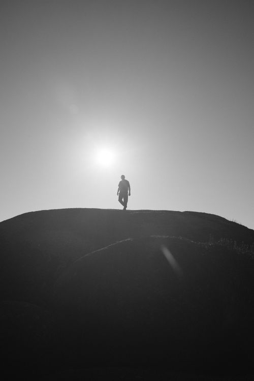 Free Silhouette of a man walking on a hilltop with the sun in the background. Stock Photo