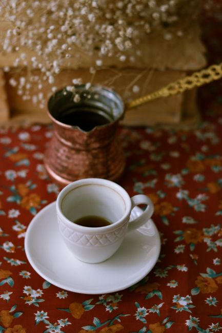 A traditional Turkish coffee set with a copper cezve and ornate cup on a floral tablecloth.