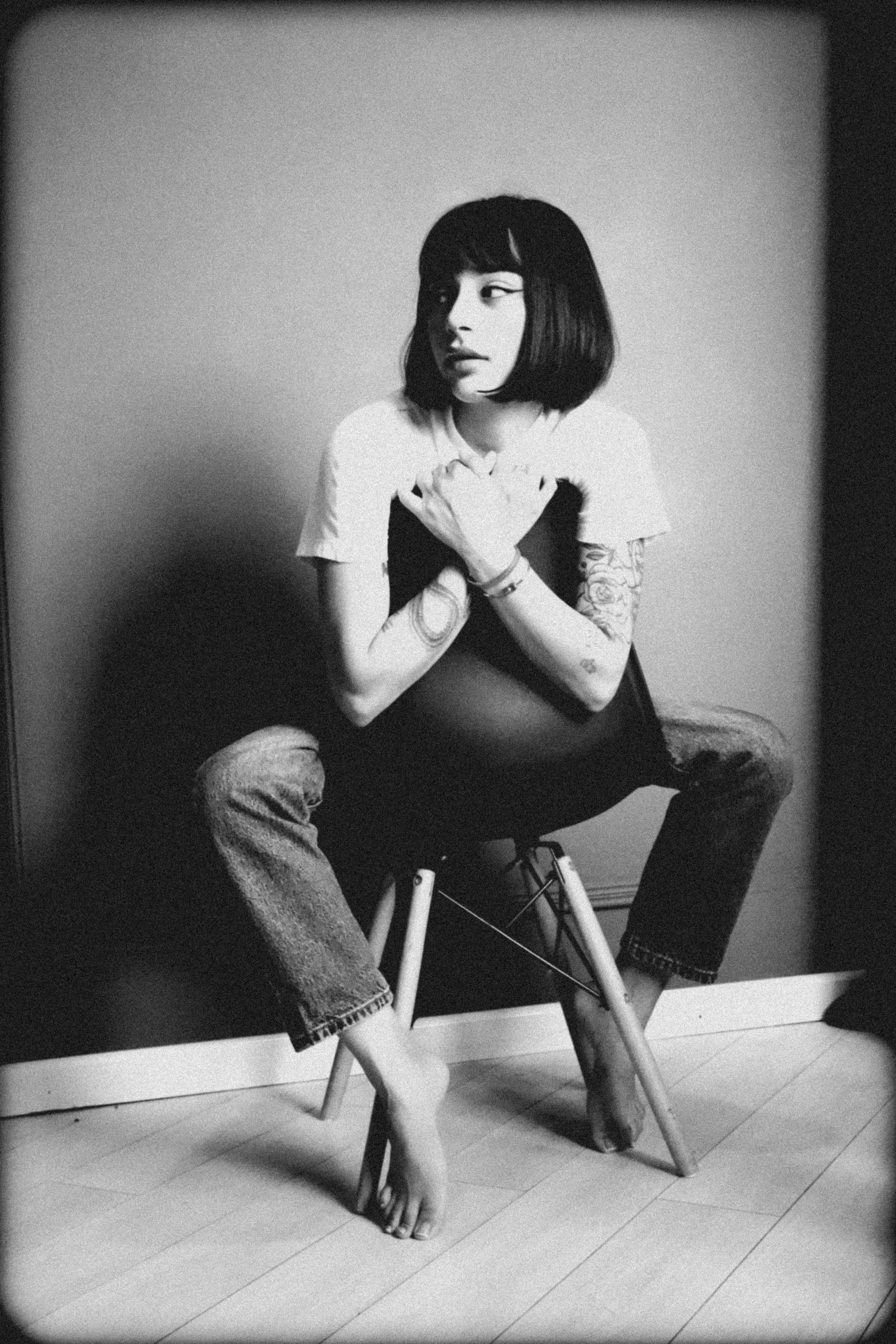 Stylish black and white portrait of a woman sitting barefoot on a chair, embodying artistic expression.