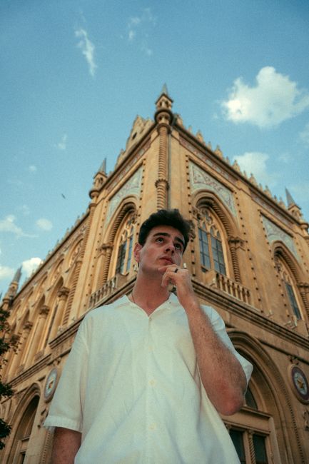 A man stands thoughtfully in front of a historic building in Baku, Azerbaijan, under a clear blue sky.