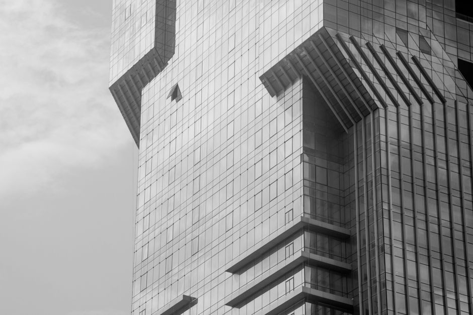 Black and white photo of a modern glass skyscraper with geometric design under a cloudy sky.