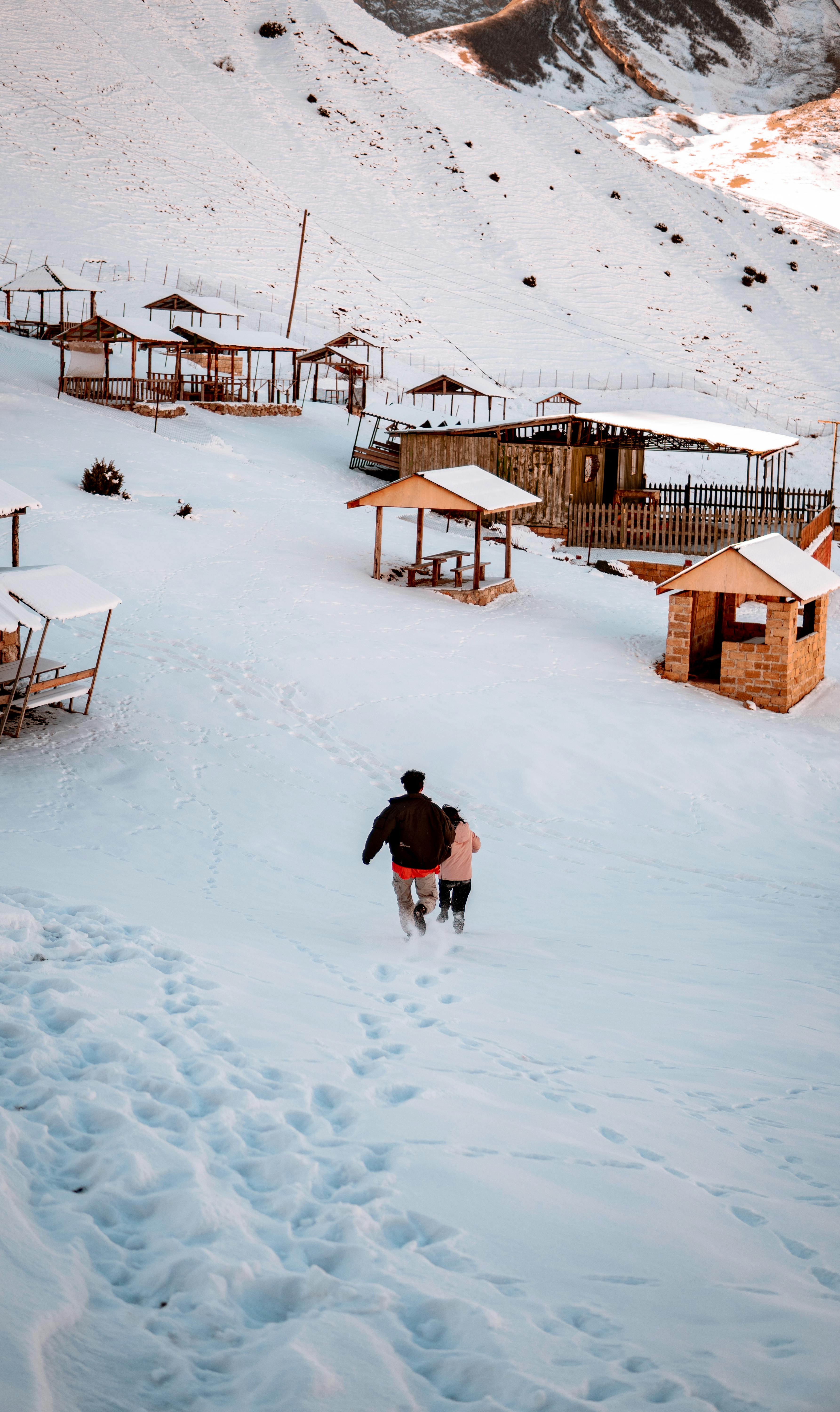 A scenic winter landscape capturing wooden huts on a snowy hillside with mountains in the background.
