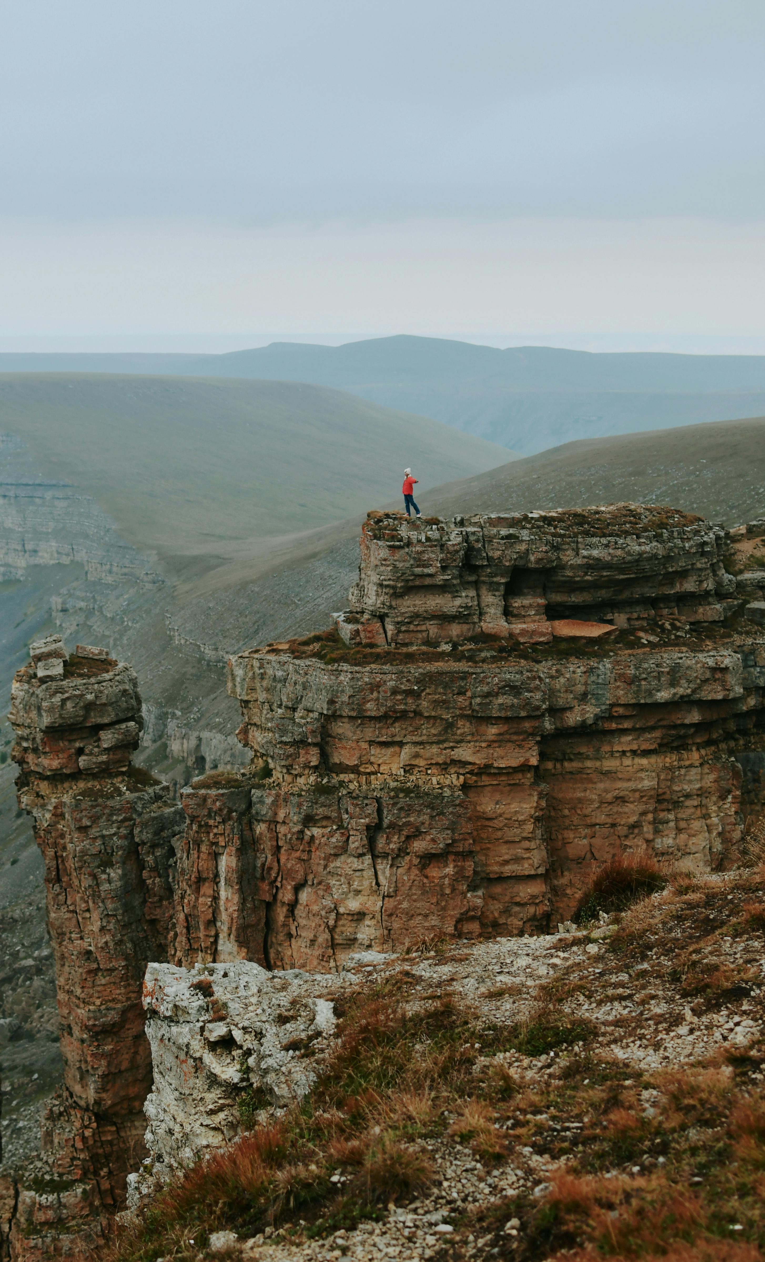A lone hiker in red stands atop a stunning rocky cliff, offering a breathtaking view.