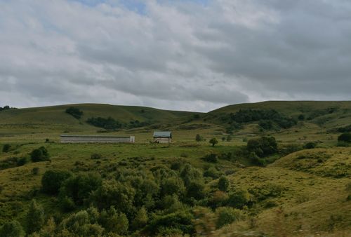 Free A tranquil countryside landscape featuring rolling hills and farm buildings under a cloudy sky. Stock Photo