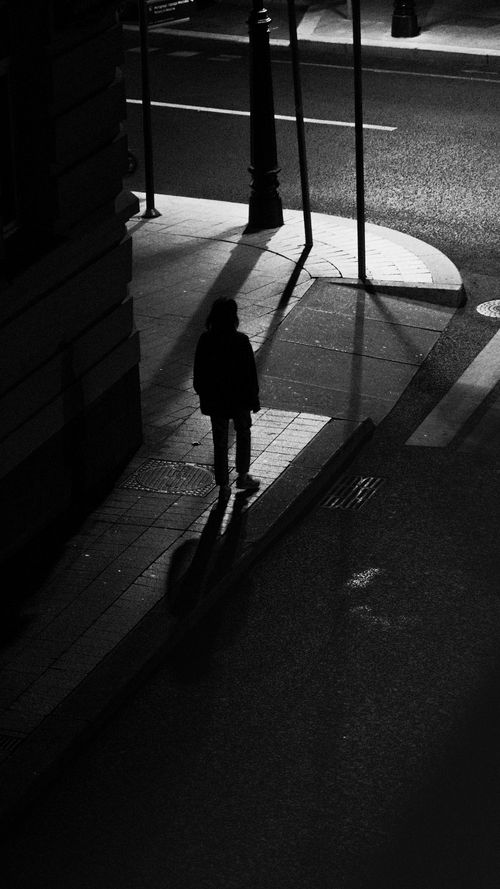 Free Silhouette of a person walking alone at night, casting a long shadow on city streets. Stock Photo