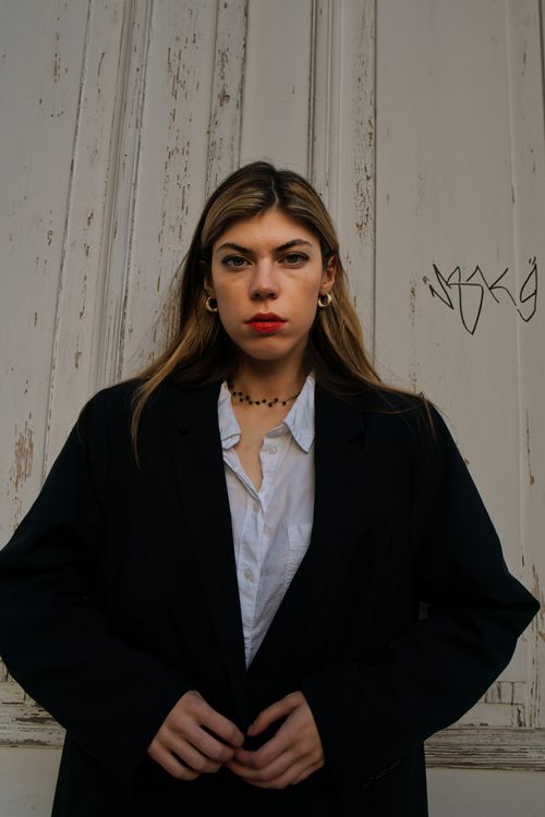 Free Elegant woman posing in a black coat with a white shirt against a textured wall. Stylish fashion portrait. Stock Photo