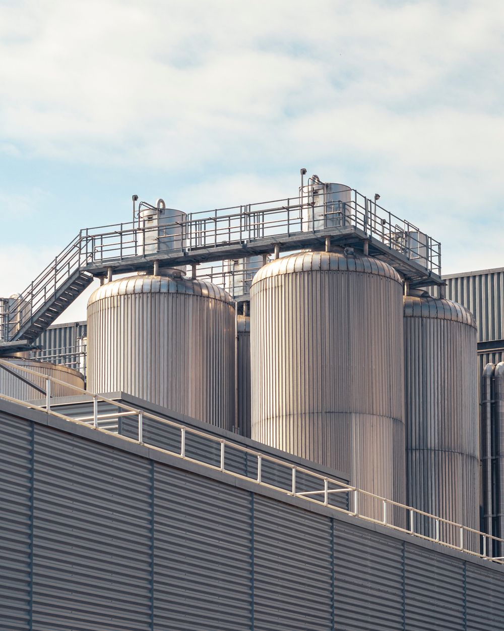 Storage tanks and process pipework at an industrial plant under a bright sky.
