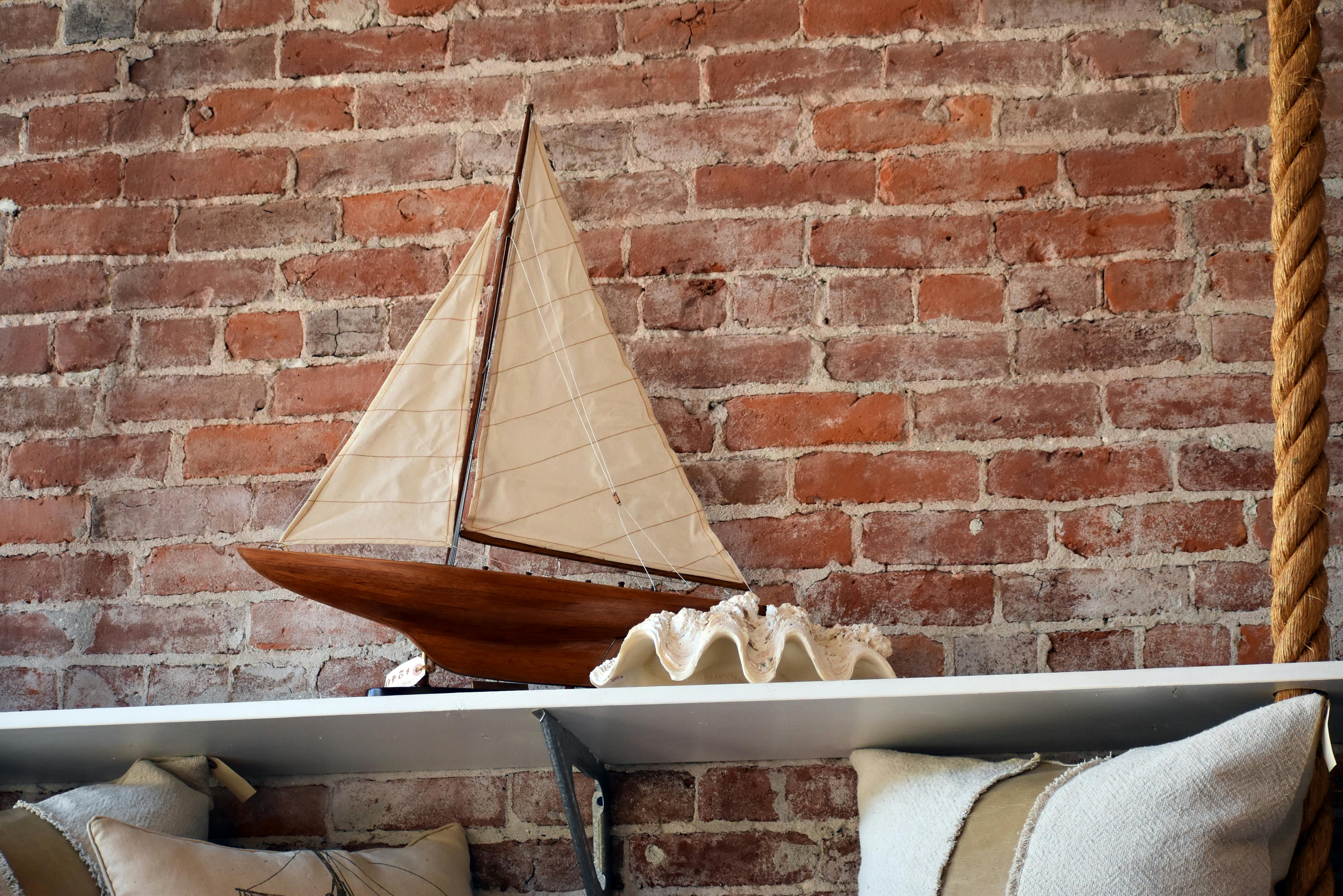Free Miniature sailboat model displayed on a shelf against a rustic brick wall adds nautical charm. Stock Photo