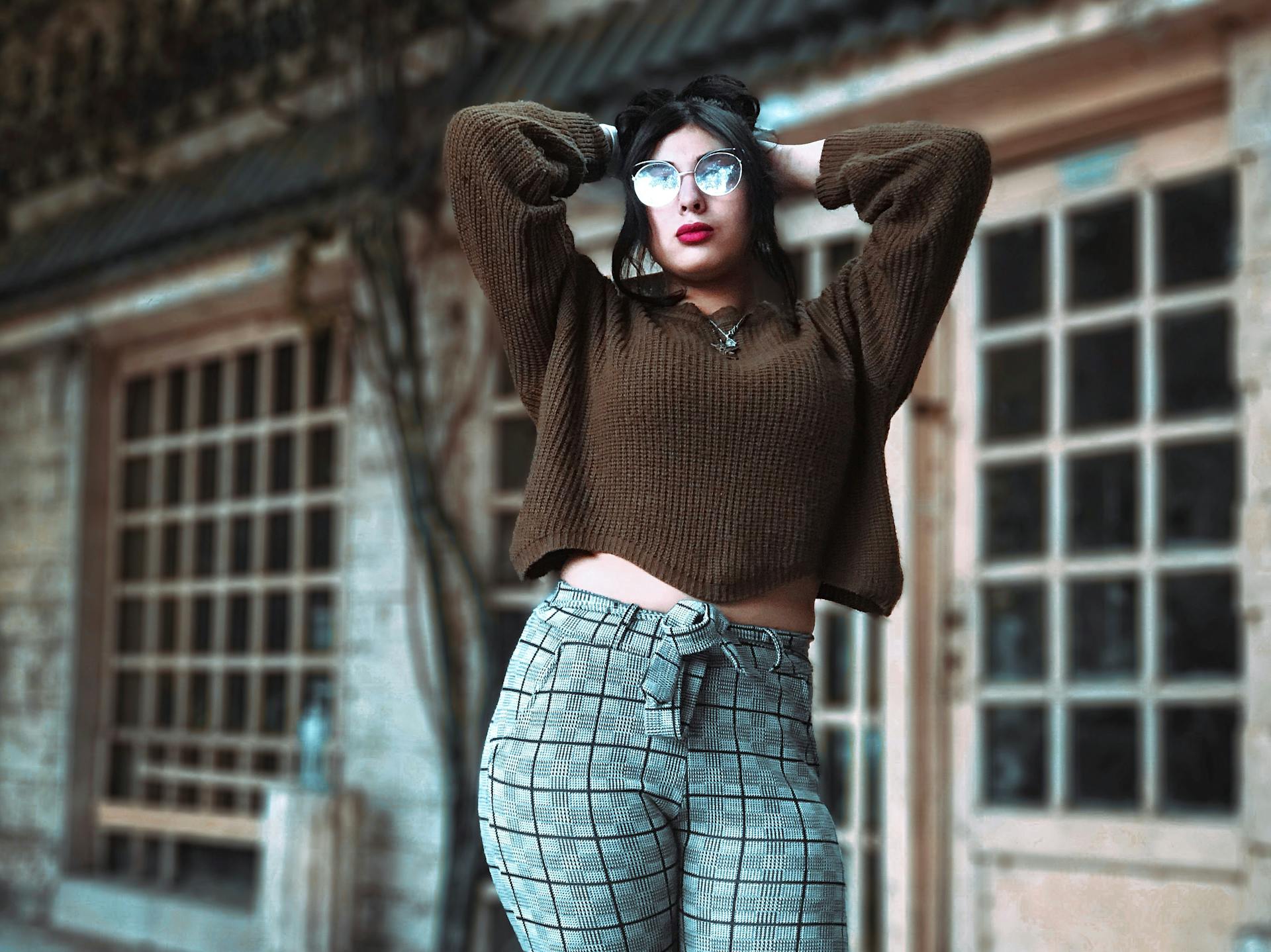 Stylish woman in glasses posing outdoors with a trendy sweater and plaid pants.