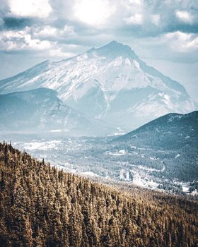A scenic view of a mountain range with forests in the foreground under a cloudy sky.